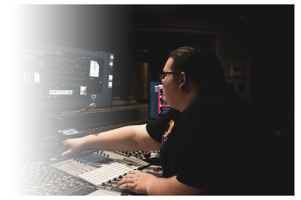 Owner, Jamie McCallum, sat reaching over a mixing desk.